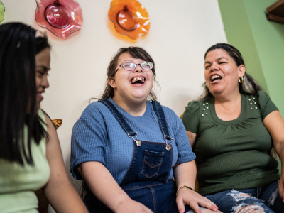 Two students and a mother sit laughing in a waiting room setting. 